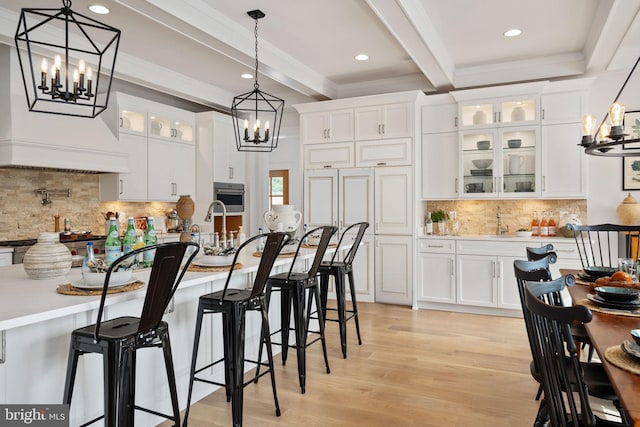 kitchen featuring a notable chandelier, beamed ceiling, oven, and white cabinetry