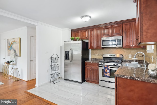 kitchen featuring appliances with stainless steel finishes, light wood-type flooring, dark stone counters, ornamental molding, and sink