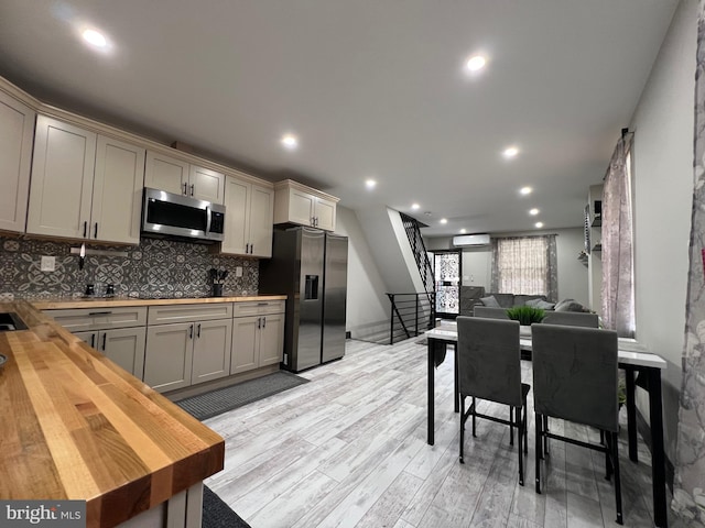 kitchen with appliances with stainless steel finishes, light hardwood / wood-style floors, backsplash, gray cabinets, and wooden counters