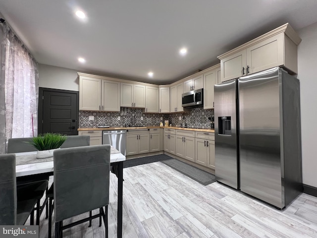 kitchen featuring cream cabinets, stainless steel appliances, light hardwood / wood-style floors, and decorative backsplash