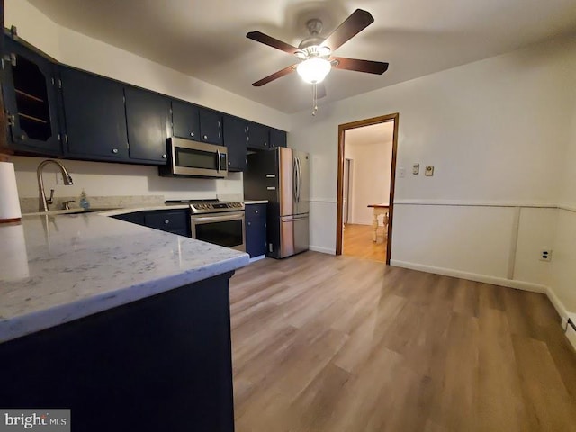 kitchen featuring light stone countertops, appliances with stainless steel finishes, sink, light wood-type flooring, and ceiling fan