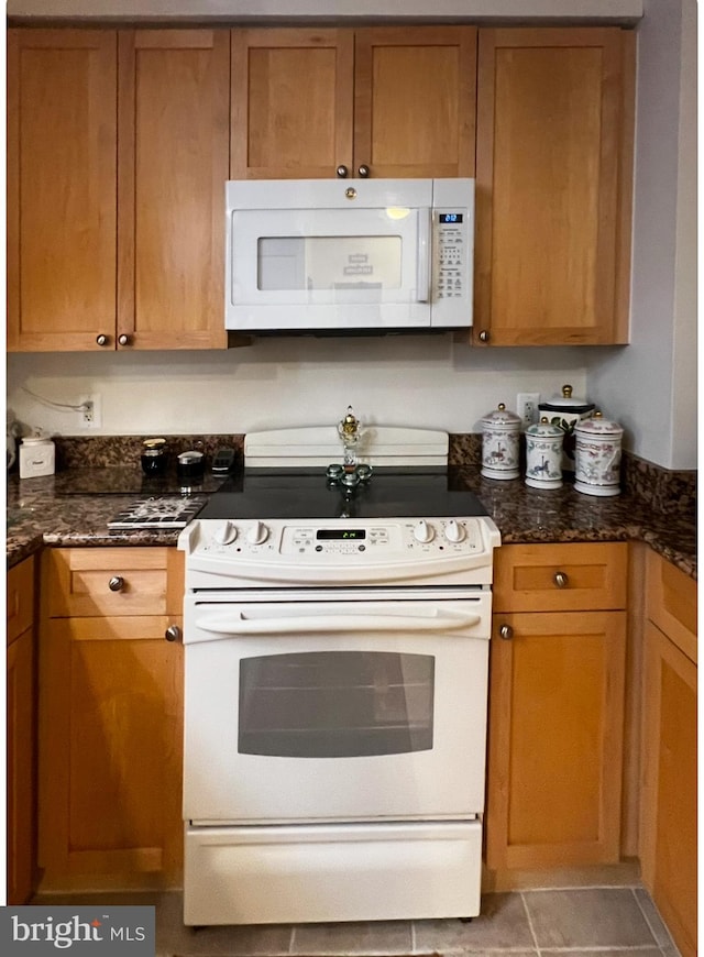 kitchen featuring dark stone countertops, white appliances, and light tile patterned floors