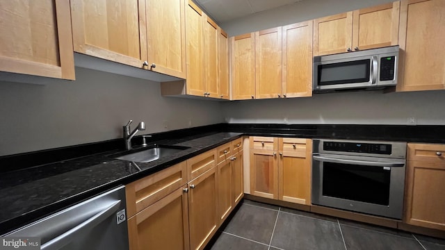 kitchen featuring appliances with stainless steel finishes, dark stone counters, sink, and dark tile patterned flooring