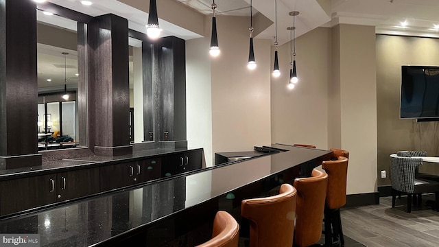 bar featuring dark brown cabinetry, pendant lighting, hardwood / wood-style flooring, and dark stone counters