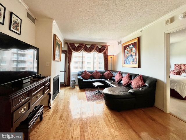 living room featuring a textured ceiling, light wood-type flooring, and ornamental molding