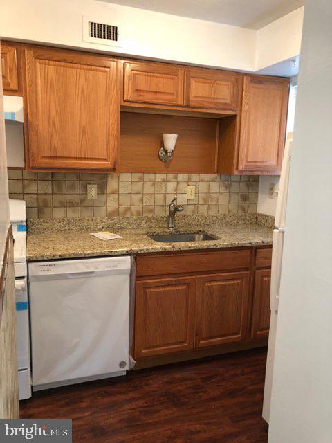 kitchen featuring dishwasher, tasteful backsplash, dark wood-type flooring, sink, and light stone countertops