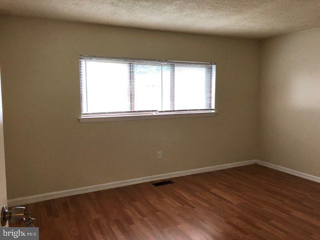 empty room featuring a textured ceiling, plenty of natural light, and dark hardwood / wood-style flooring