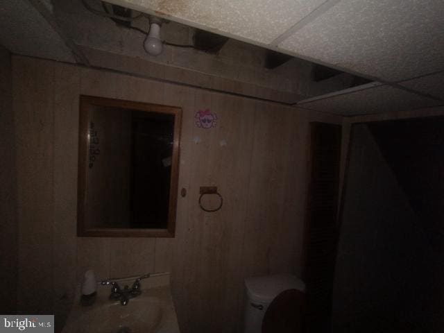 bathroom with wood walls, toilet, and a paneled ceiling