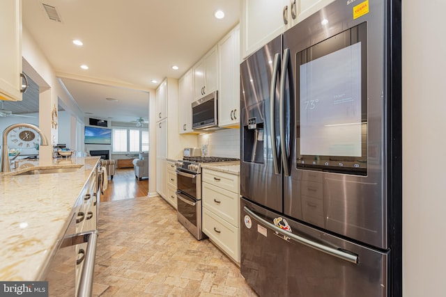 kitchen featuring white cabinets, sink, stainless steel appliances, light stone countertops, and decorative backsplash