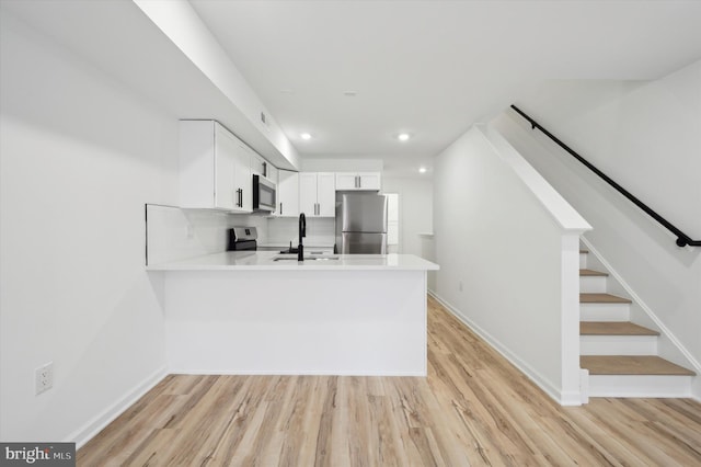 kitchen with light hardwood / wood-style flooring, stainless steel appliances, white cabinetry, and kitchen peninsula