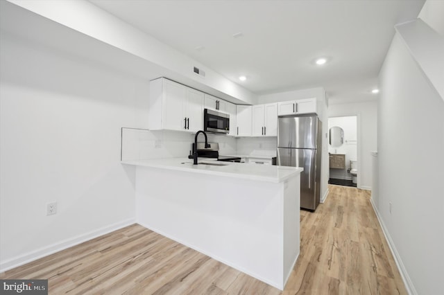 kitchen with light hardwood / wood-style floors, white cabinets, kitchen peninsula, decorative backsplash, and appliances with stainless steel finishes