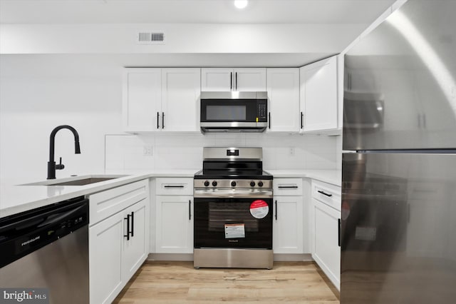 kitchen with sink, white cabinetry, appliances with stainless steel finishes, light hardwood / wood-style floors, and decorative backsplash