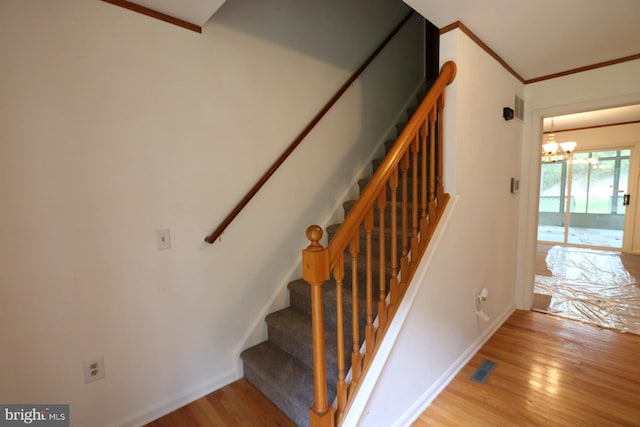 stairs with an inviting chandelier, crown molding, and hardwood / wood-style floors