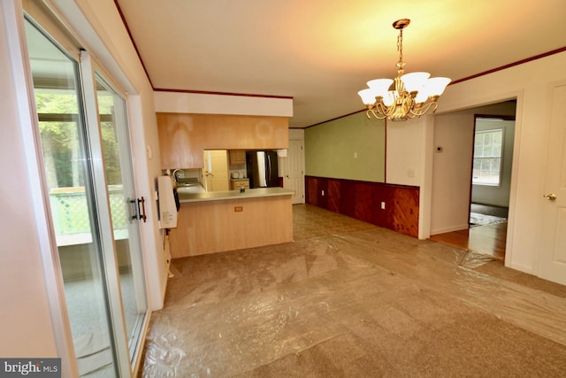 kitchen featuring a chandelier, kitchen peninsula, stainless steel refrigerator, wooden walls, and decorative light fixtures