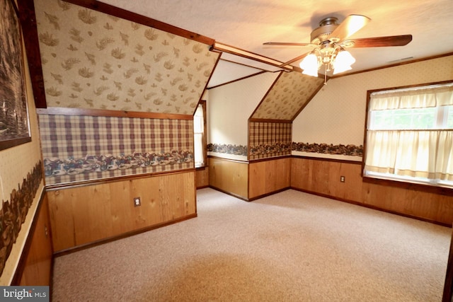 bonus room with ceiling fan, a textured ceiling, wood walls, and light carpet