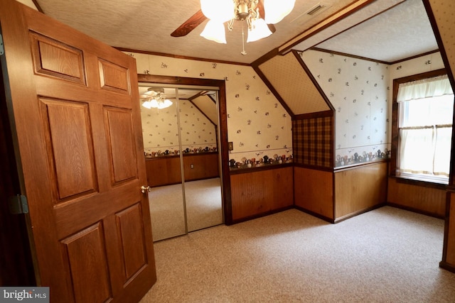 interior space featuring ceiling fan, a textured ceiling, wooden walls, and light carpet