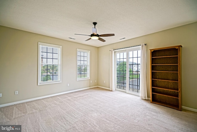 spare room featuring a healthy amount of sunlight, ceiling fan, light colored carpet, and a textured ceiling