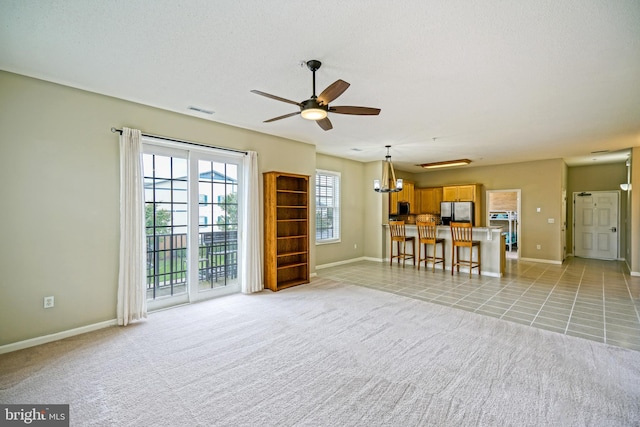 unfurnished living room featuring light carpet and ceiling fan with notable chandelier