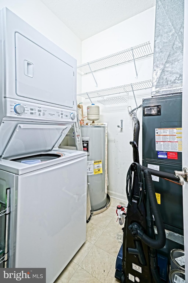 laundry area with electric water heater, light tile patterned floors, and stacked washer and clothes dryer