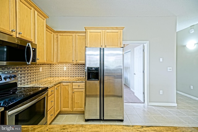 kitchen with light brown cabinets, backsplash, light tile patterned floors, light stone countertops, and appliances with stainless steel finishes