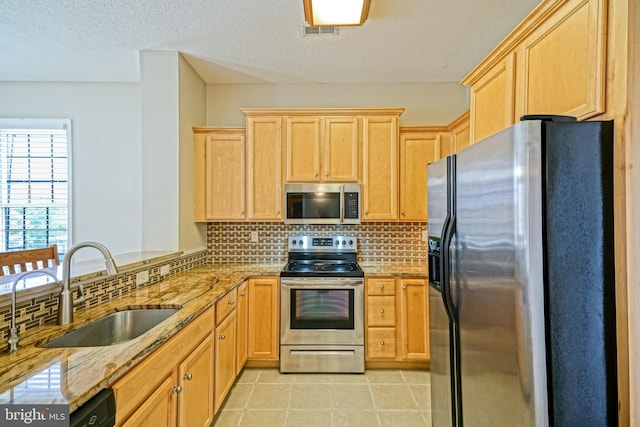 kitchen with backsplash, sink, light stone countertops, appliances with stainless steel finishes, and light tile patterned flooring