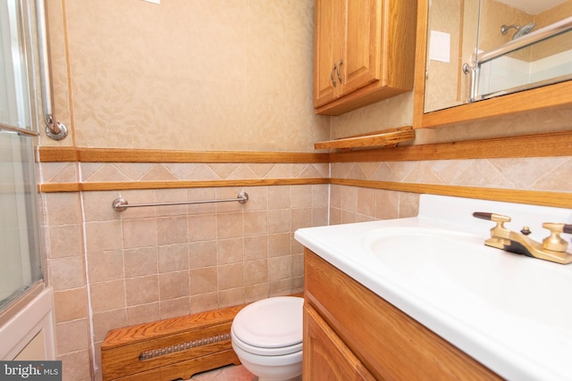 bathroom featuring vanity, a shower with door, toilet, and tile walls