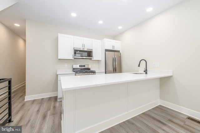 kitchen with appliances with stainless steel finishes, sink, kitchen peninsula, and white cabinetry