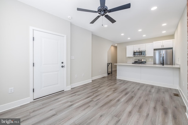 kitchen with ceiling fan, kitchen peninsula, white cabinetry, stainless steel appliances, and light wood-type flooring