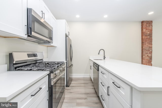 kitchen with appliances with stainless steel finishes, white cabinets, kitchen peninsula, light hardwood / wood-style flooring, and sink