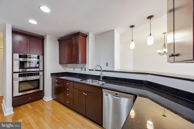 kitchen with a sink, dark stone counters, decorative light fixtures, light wood-type flooring, and appliances with stainless steel finishes