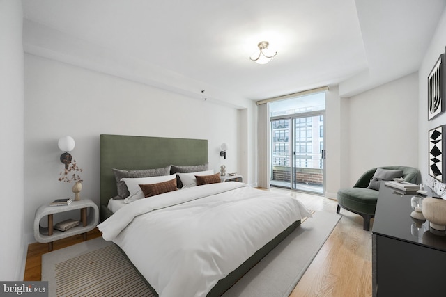 bedroom featuring expansive windows, light wood-style flooring, and access to outside