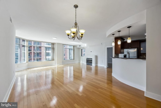 unfurnished living room featuring baseboards, light wood-style floors, and a chandelier
