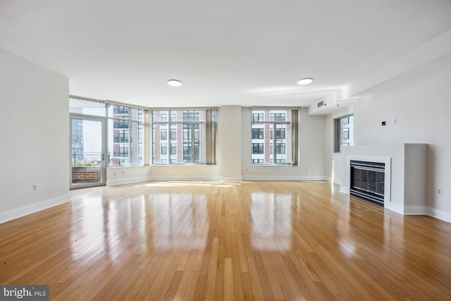 unfurnished living room featuring baseboards, light wood-style floors, and a glass covered fireplace