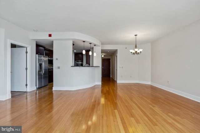 unfurnished living room featuring a notable chandelier, light wood-type flooring, and baseboards