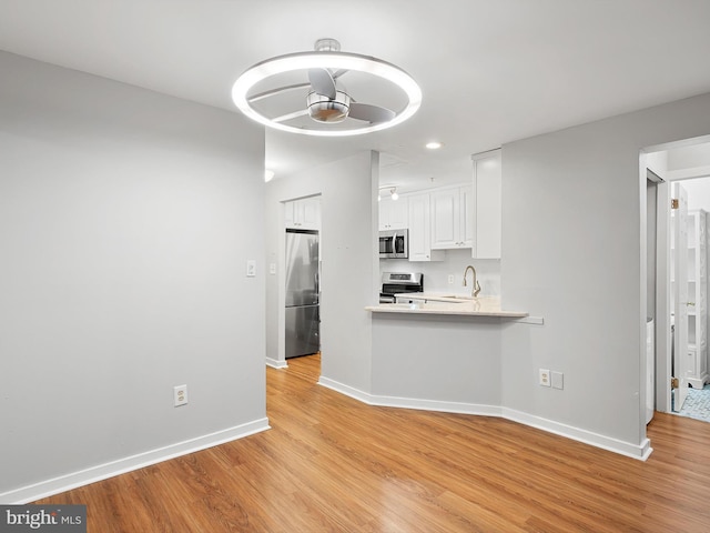 kitchen featuring sink, kitchen peninsula, white cabinetry, appliances with stainless steel finishes, and light wood-type flooring