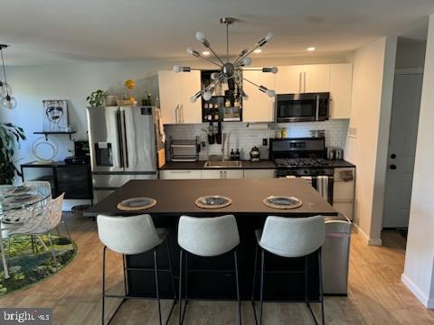 kitchen featuring sink, white cabinetry, light hardwood / wood-style flooring, stainless steel appliances, and backsplash