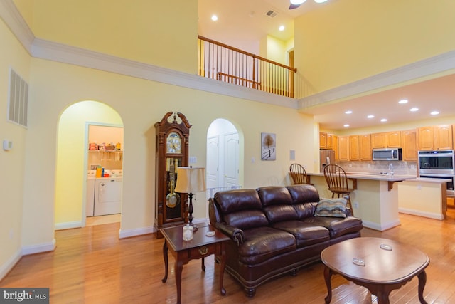 living room featuring light wood-type flooring, sink, independent washer and dryer, crown molding, and a high ceiling