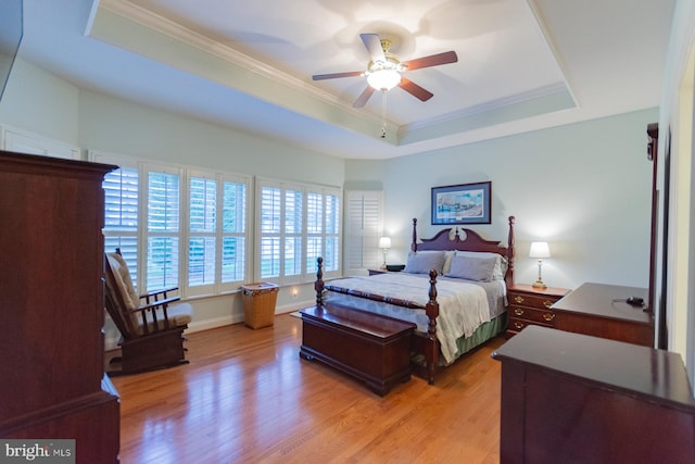 bedroom featuring light wood-type flooring, ceiling fan, a raised ceiling, and crown molding