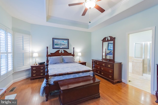 bedroom featuring ceiling fan, connected bathroom, a tray ceiling, light wood-type flooring, and crown molding