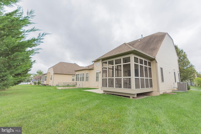 rear view of house with cooling unit, a sunroom, and a lawn