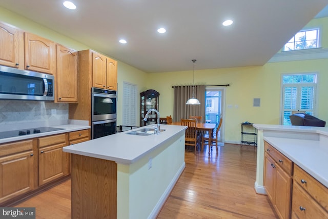 kitchen featuring sink, an island with sink, light hardwood / wood-style flooring, appliances with stainless steel finishes, and decorative light fixtures