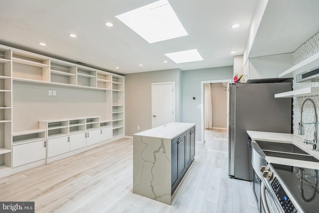 kitchen with light stone countertops, a skylight, stainless steel appliances, and light hardwood / wood-style floors