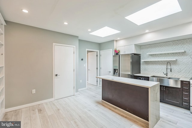 kitchen with sink, dark brown cabinets, backsplash, stainless steel refrigerator with ice dispenser, and light wood-type flooring