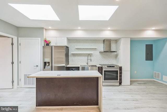 kitchen featuring a skylight, sink, wall chimney range hood, white cabinetry, and appliances with stainless steel finishes