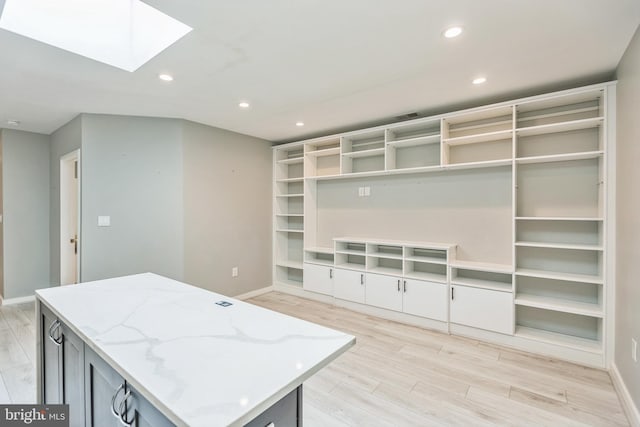 interior space with light wood-type flooring, a kitchen island, light stone countertops, and a skylight