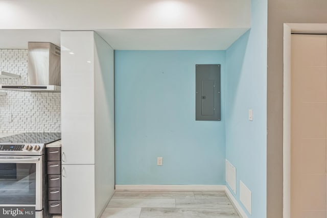 kitchen featuring light hardwood / wood-style floors, electric panel, wall chimney exhaust hood, backsplash, and stainless steel range with electric stovetop