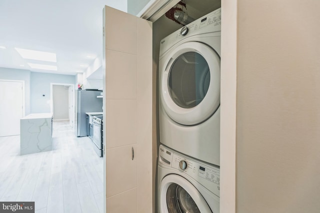 clothes washing area with light hardwood / wood-style flooring and stacked washer and dryer