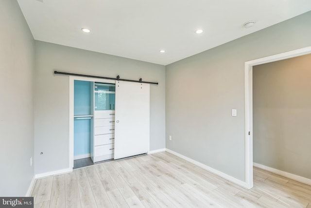 unfurnished bedroom featuring a closet, a barn door, and light hardwood / wood-style flooring