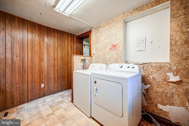 clothes washing area featuring washer and clothes dryer and wood walls