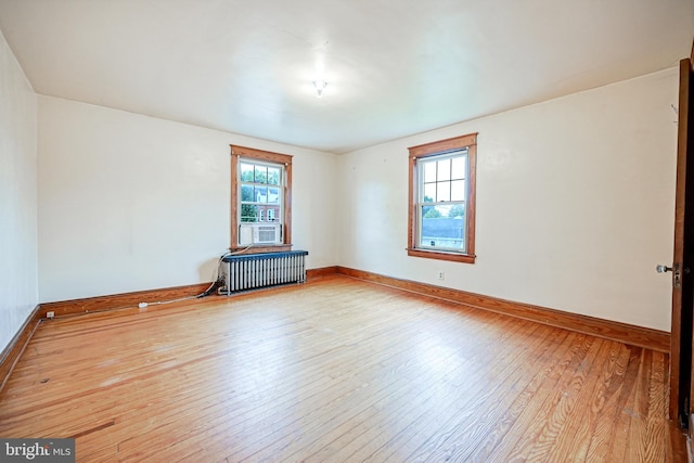 empty room featuring light wood-type flooring, cooling unit, radiator heating unit, and plenty of natural light